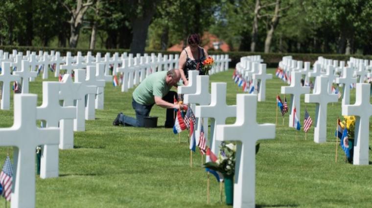 A man and woman place flowers at a headstone.