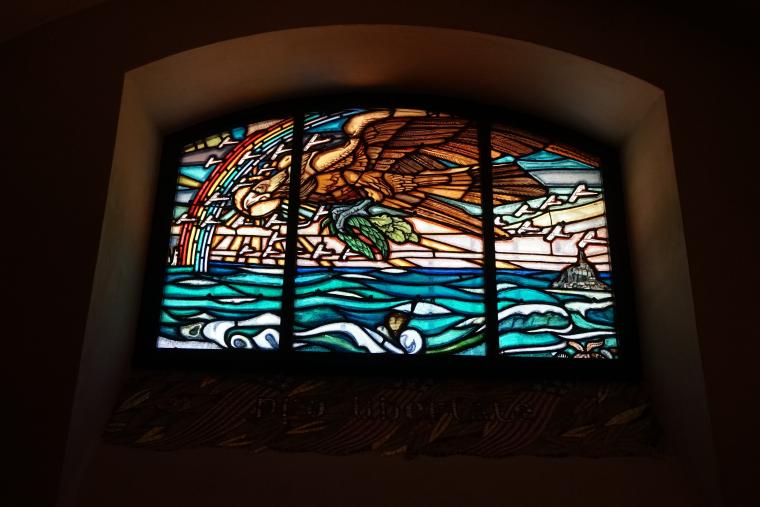 An eagle, surrounded by planes, flies over the water in this stained-glass window.