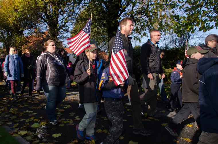 Boy Scouts carry American flags as they enter the cemetery.