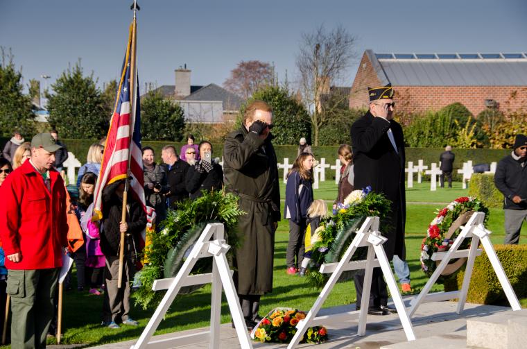 Two men stand and salute after laying floral wreaths.