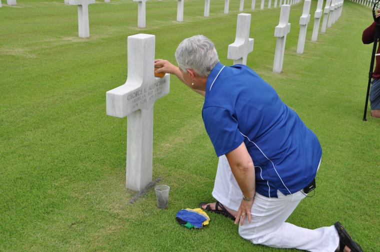 Touzel kneels on the ground as she takes a sponge to the headstone.