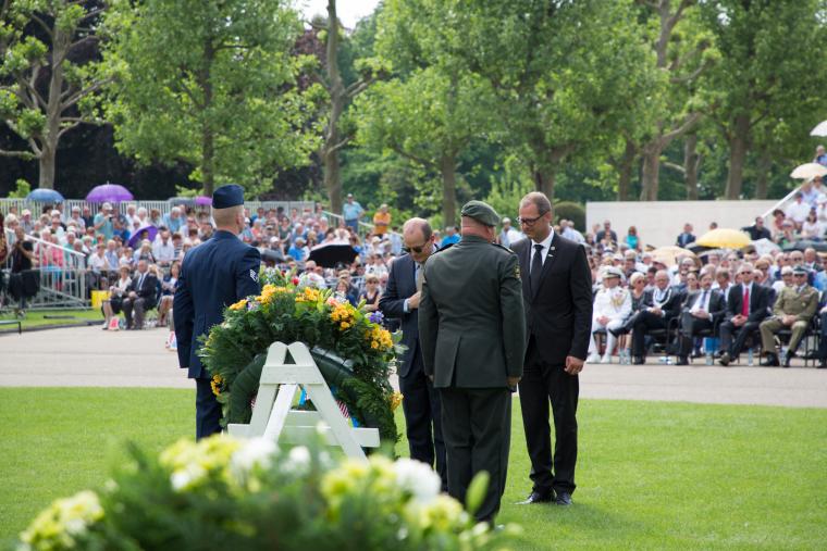 Men in suits pause after laying a floral wreath.