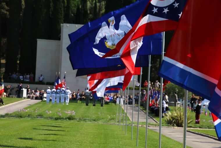 Large, state flags flap in the wind during the ceremony. 