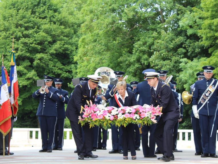 Men and a woman carry a large floral wreath together. 