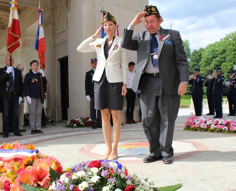 A man and woman salute after laying a wreath. 