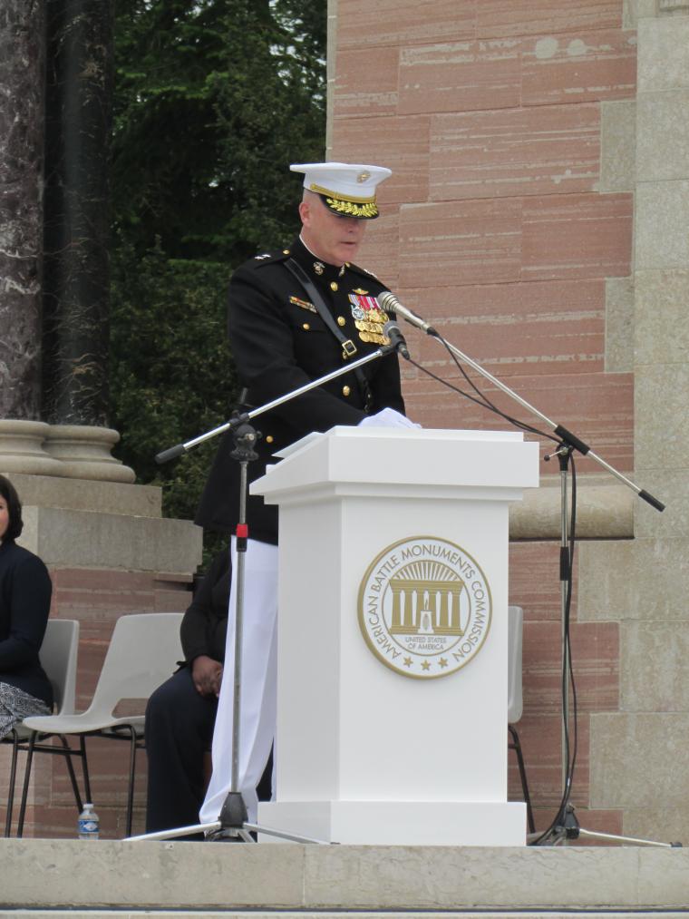 A man in a Marine uniform speaks from a podium. 