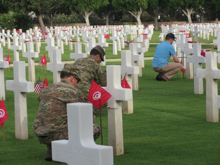 Volunteers kneel down to place American and Tunisian flags in the ground. 