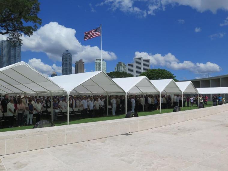Attendees stand under a tent during the ceremony. 