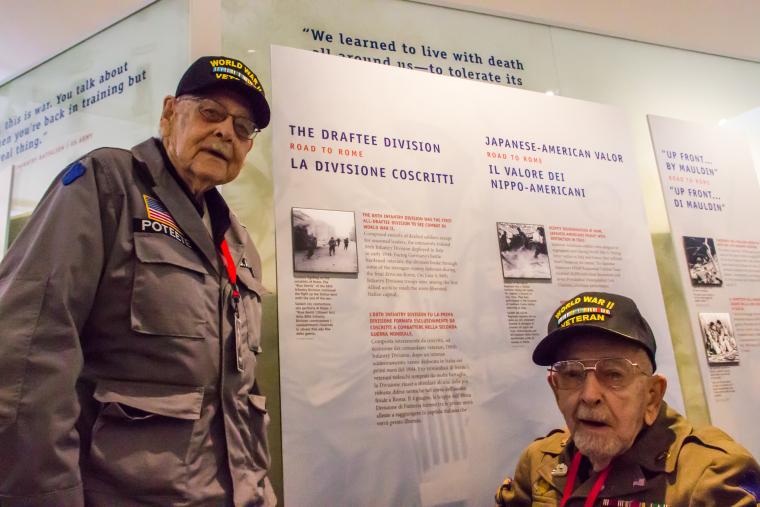 WWII veterans Poteete and Spencer stand next to a panel about the 88th Infantry Division. 