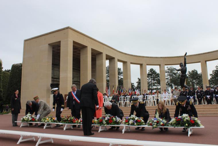 Men and women kneel down to place floral wreaths on wooden stands. 