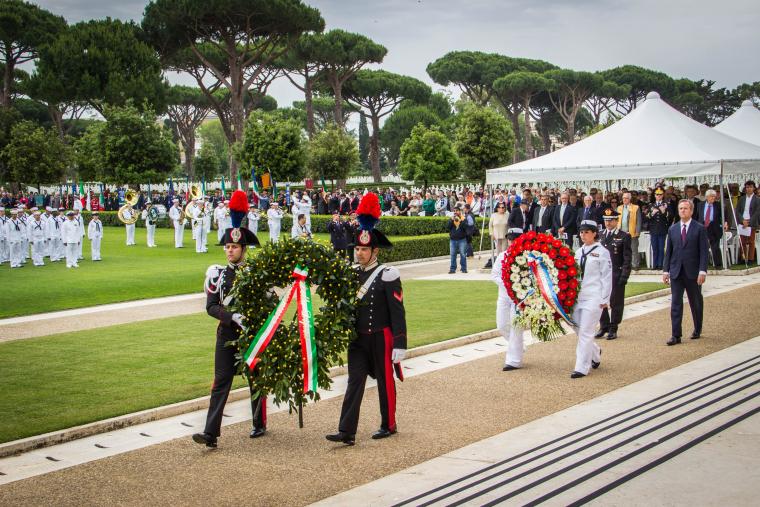 Men and women in uniform carry large floral wreaths. 