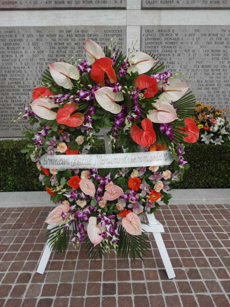 A large floral wreath on a wooden stand rests in front of the Tablets of the Missing. 