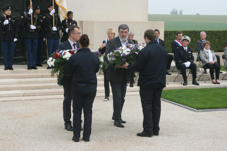 Two men in suits prepare to lay floral wreaths.