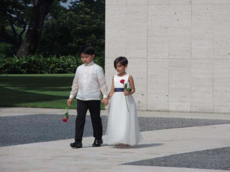 A young boy and girl each carry a single red rose. 