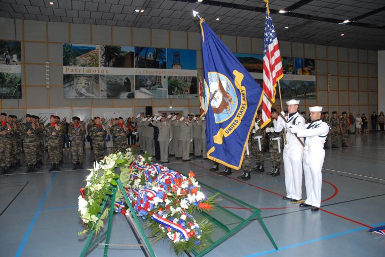 Two sailors stand over the floral wreaths with flags.