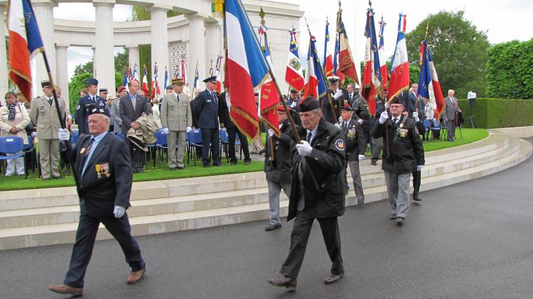 Men with flags walk in front of the memorial. 