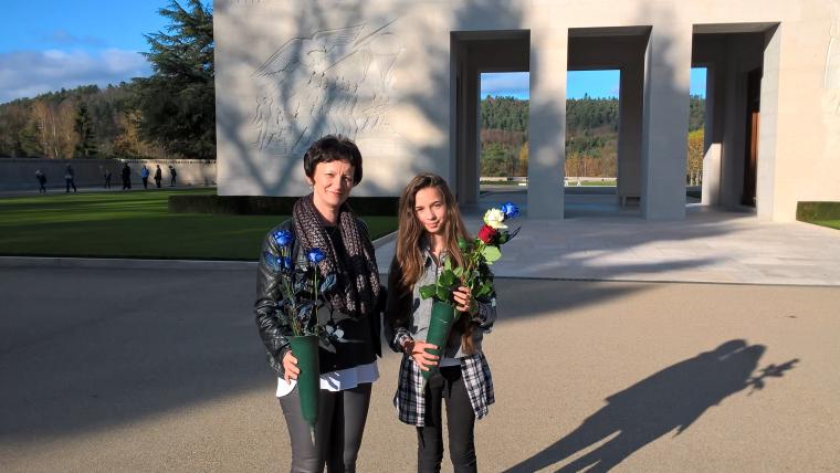Woman and girl stand with roses, ready to place them at a headstone.
