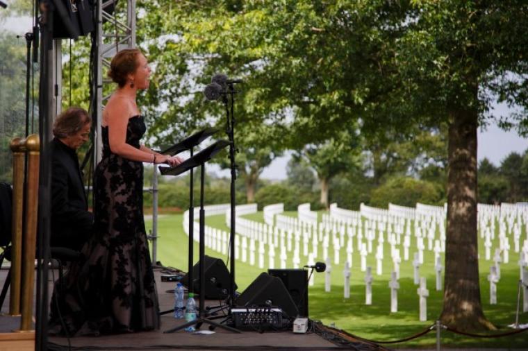A woman in a dress sings into a microphone with headstones in the background.