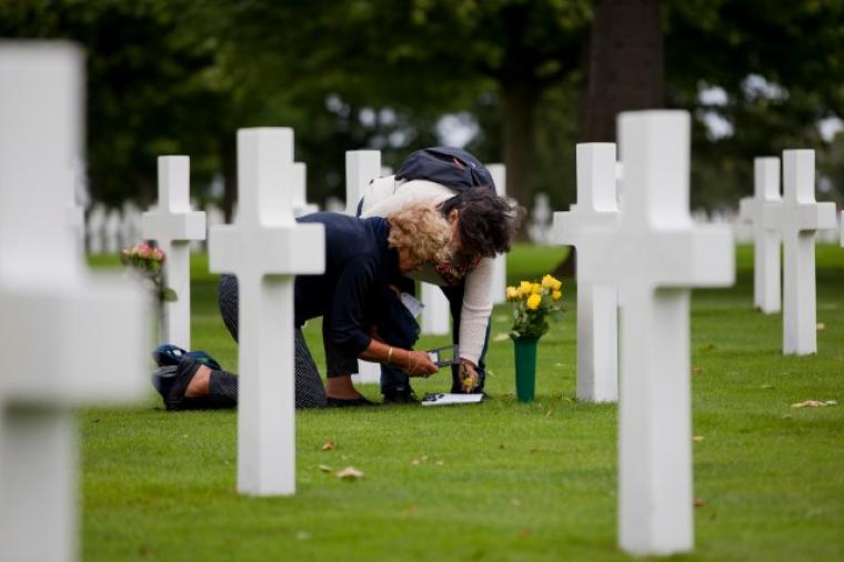 Two women prepare flowers for placement at a headstone. 